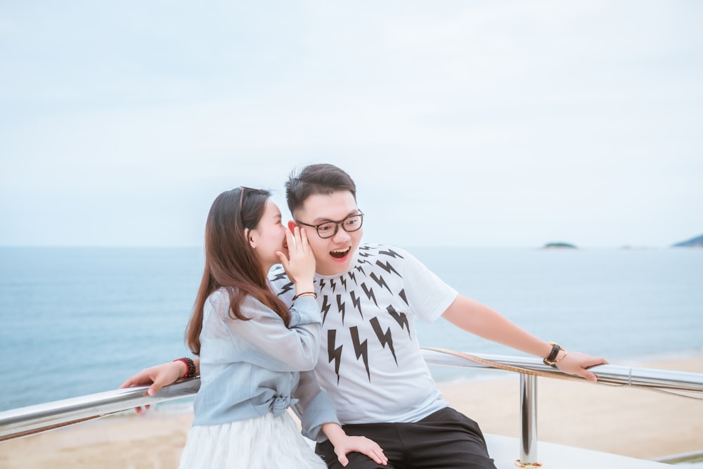 woman whispering to man's ear near sea