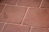 A close-up view of terracotta floor tiles with a slightly rough texture. The tiles are arranged in a grid pattern with visible grout lines in between.