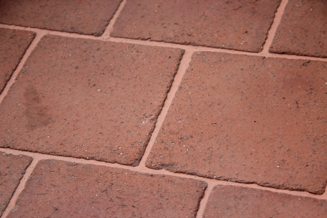 A close-up view of terracotta floor tiles with a slightly rough texture. The tiles are arranged in a grid pattern with visible grout lines in between.