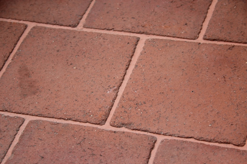 A close-up view of terracotta floor tiles with a slightly rough texture. The tiles are arranged in a grid pattern with visible grout lines in between.