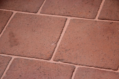 A close-up view of terracotta floor tiles with a slightly rough texture. The tiles are arranged in a grid pattern with visible grout lines in between.