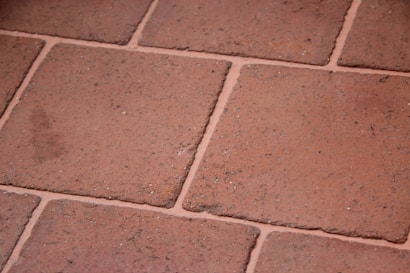 A close-up view of terracotta floor tiles with a slightly rough texture. The tiles are arranged in a grid pattern with visible grout lines in between.
