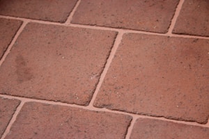 A close-up view of terracotta floor tiles with a slightly rough texture. The tiles are arranged in a grid pattern with visible grout lines in between.