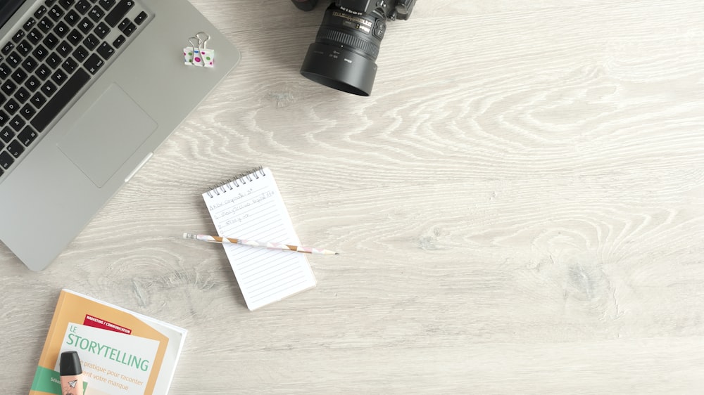 DSLR camera beside laptop and pen on notebook