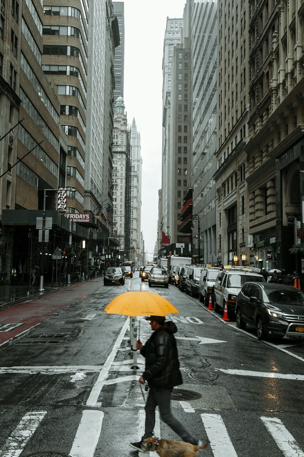 uomo che indossa una giacca a bolle nera che tiene l'ombrello giallo che attraversa la strada