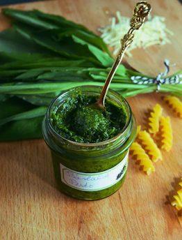 A spoon scooping bright green chimi gel from a glass jar with fresh parsley in the background