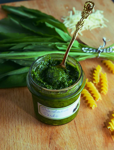 Close-up of a jar of traditional Sicilian pesto with fresh basil leaves and pine nuts.
