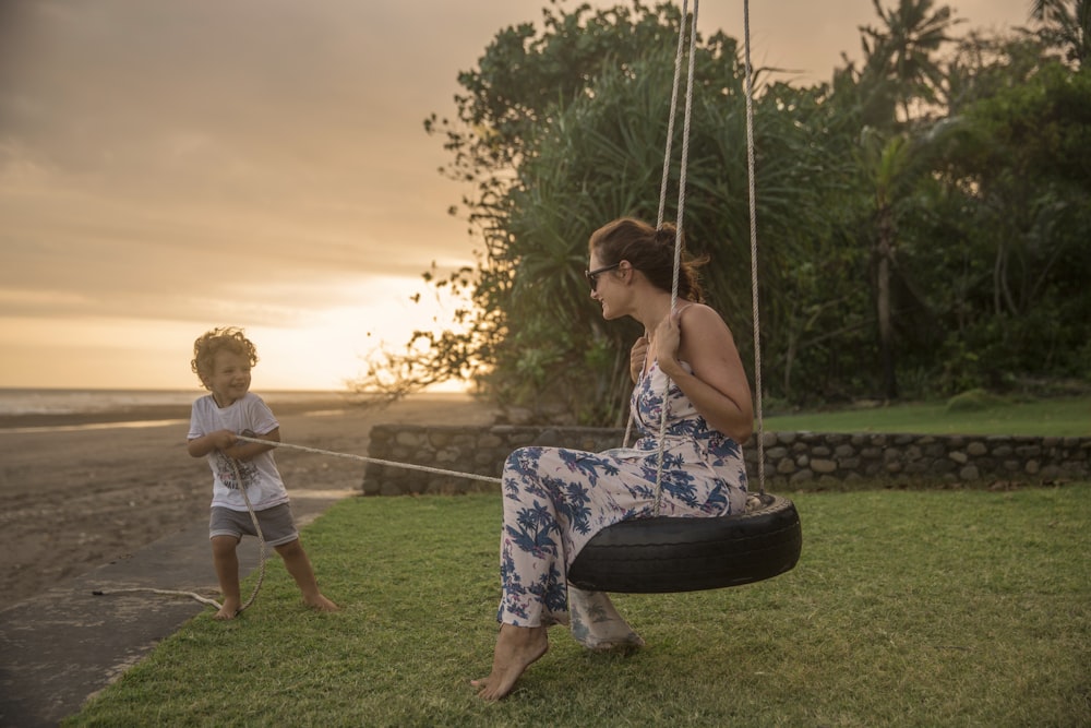 woman on tire swing pulled by boy