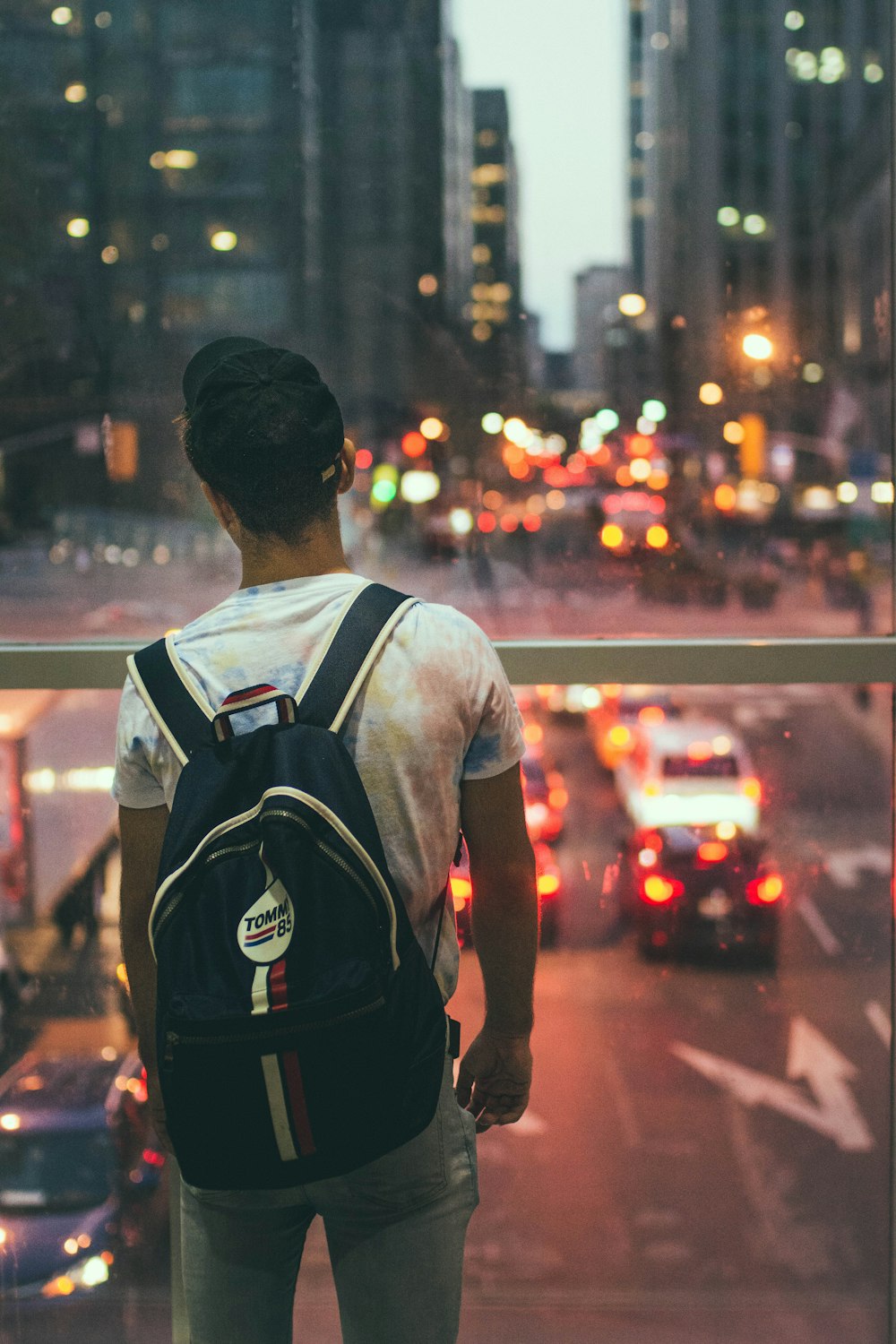 man wearing white shirt wearing black backpack staring at busy street