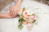 Close-up of wedding rings resting on a silk ribbon beside a bouquet of white roses.