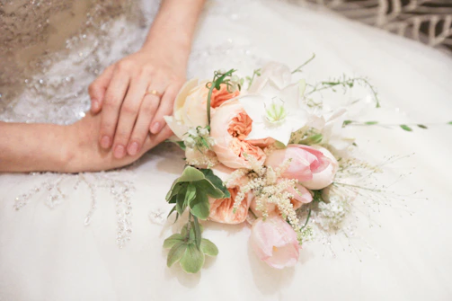 Close-up of wedding rings resting on a silk ribbon beside a bouquet of white roses.