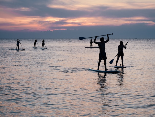 Group of friends enjoying paddleboarding on calm, clear waters during sunset