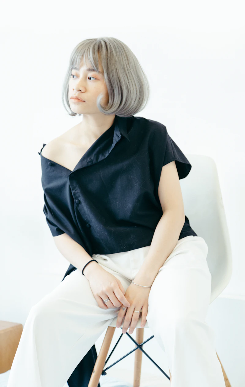 Fashion model in black blouse seated on stool, white backdrop
