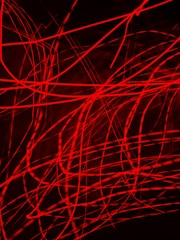 Red laser-like lines crisscross against a dark background, creating an abstract and dynamic pattern.