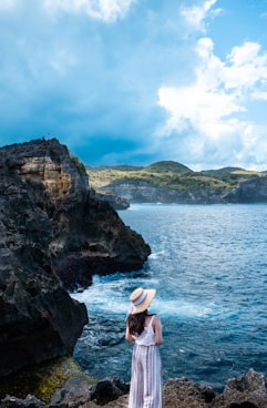 woman wearing white rompers standing on rock overlooking on the ocean