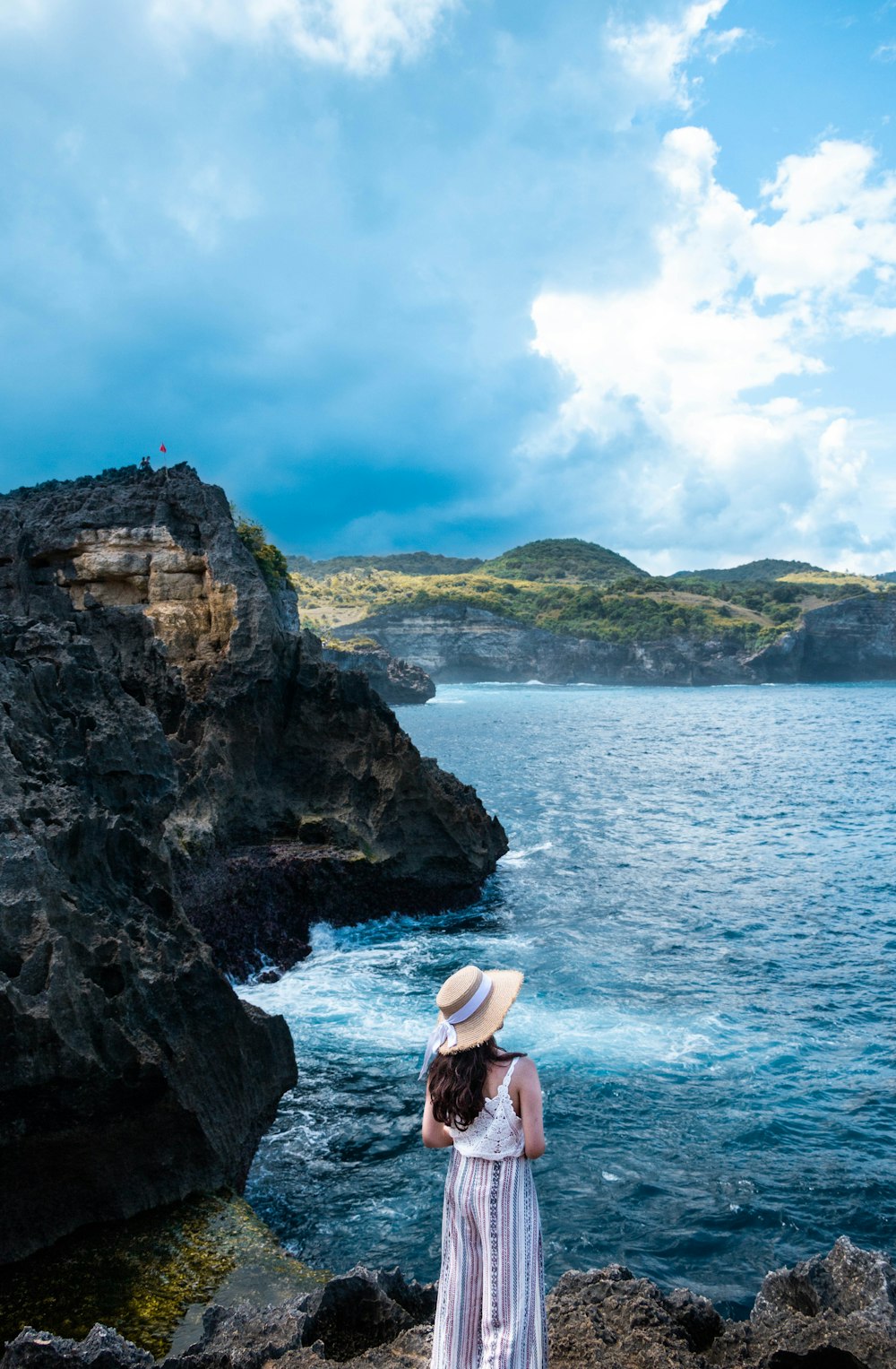 woman wearing white rompers standing on rock overlooking on the ocean