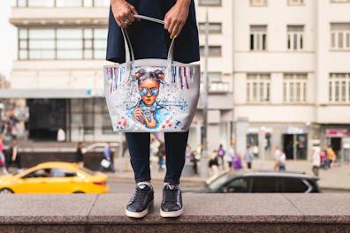 A casual canvas tote bag with bold streetwear graphics hanging from a bicycle handlebar.