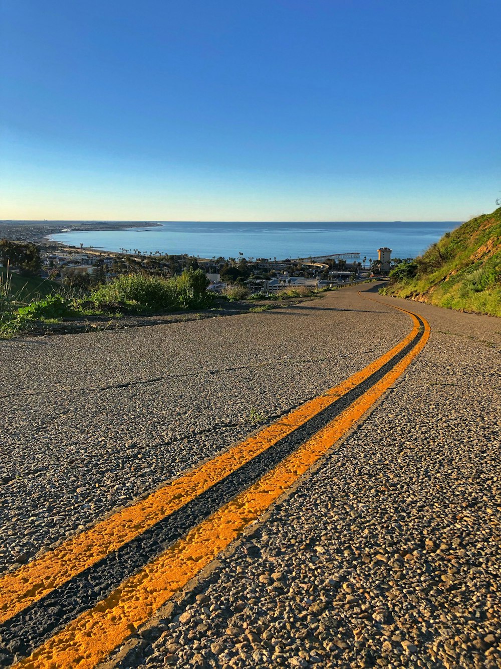 estrada de concreto cinza vendo o mar azul sob céus azuis e brancos