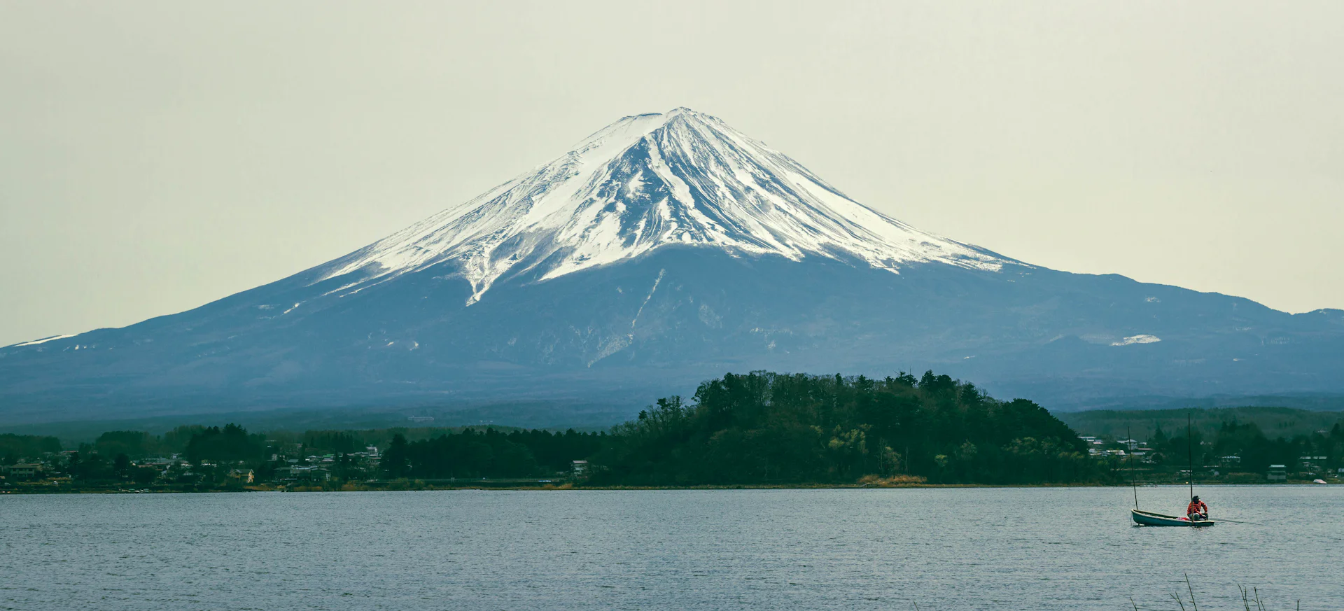 Snow-capped Mount Fuji above a calm lake with a small boat
