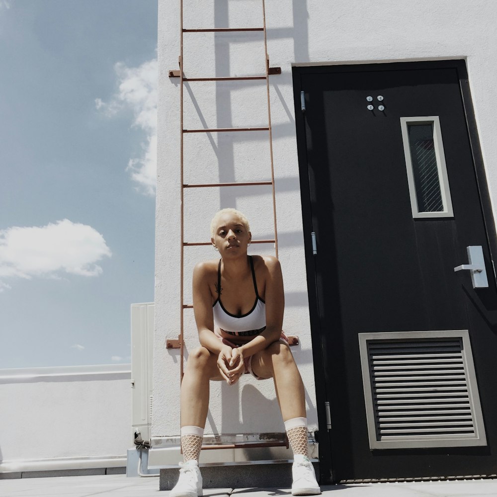 woman in white and black sports bra sitting on orange metal fire ladder