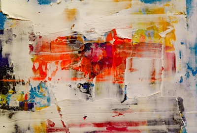 An abstract painting featuring a textured surface with bold strokes and layered colors. Dominant colors include vibrant reds and oranges, blended with patches of blue, yellow, and white. The composition appears dynamic, with a sense of movement conveyed through the brushstrokes and color transitions.