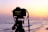 A filmmaker capturing a sunset scene with a vintage camera on a quiet beach.