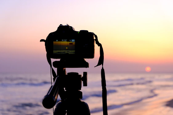 A warm, golden-lit photo of a videographer filming a sunset over the San Francisco Bay, with a microphone and camera gear nearby.