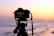 A filmmaker capturing a sunset scene with a vintage camera on a quiet beach.