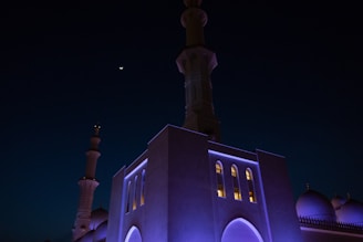 A serene mosque entrance illuminated by soft lantern light under a crescent moon.