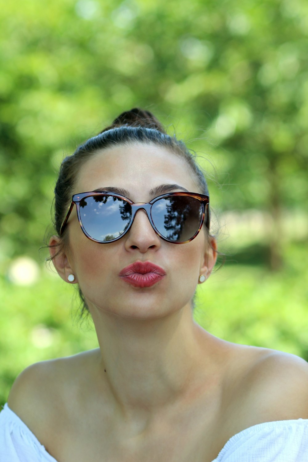 shallow focus photo of woman in white off-shoulder top wearing black sunglasses