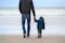 man and boy walking on seashore under blue sky