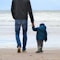man and boy walking on seashore under blue sky