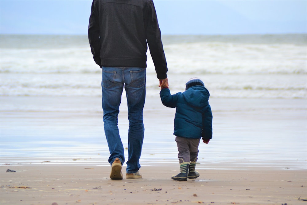 man and boy walking on seashore under blue sky