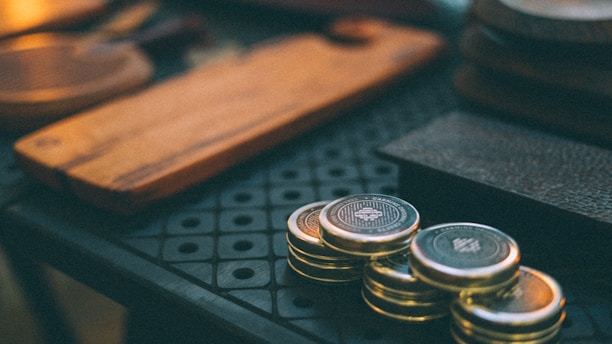 Close-up of gold coins stacked beside survival gear on a rustic wooden table.