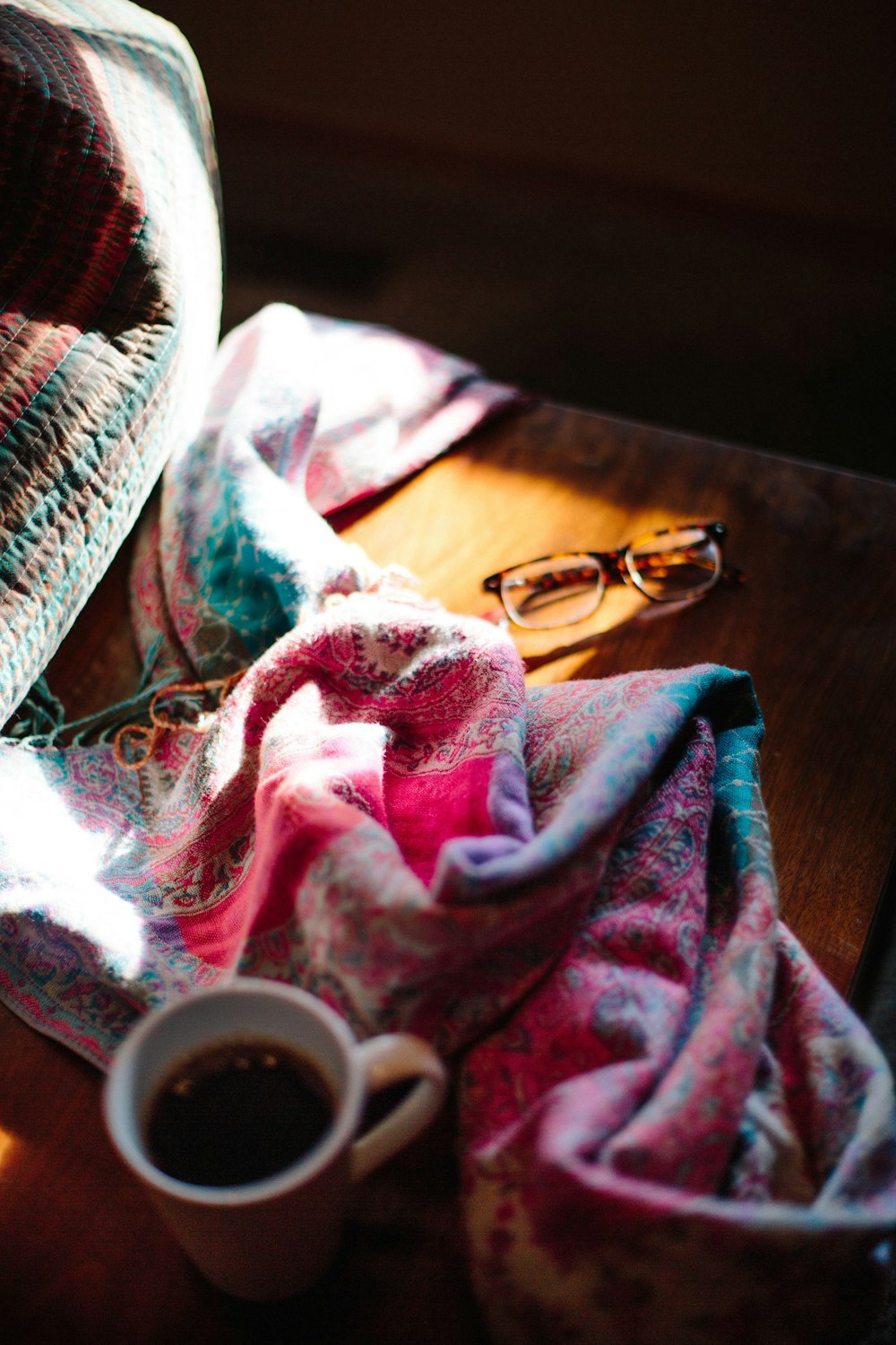 eyeglasses beside blanket and beverage filled mug