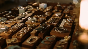 A collection of various pieces of jewelry, including rings, bracelets, and necklaces, displayed on wooden blocks. The arrangement is illuminated with warm lighting, creating a cozy and inviting atmosphere.