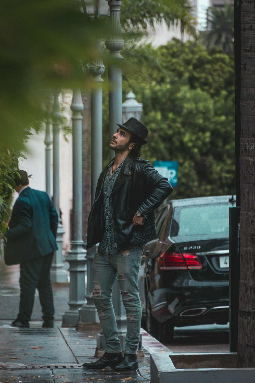 man wearing black jacket and hat standing beside road