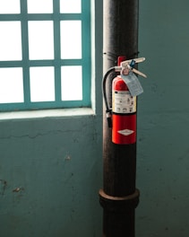 red fire extinguisher on brown metal pipe near window