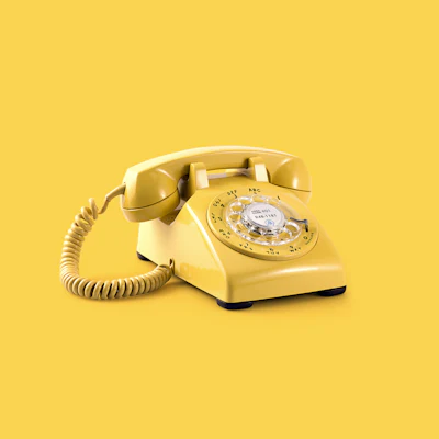 Yellow rotary telephone on a plain background