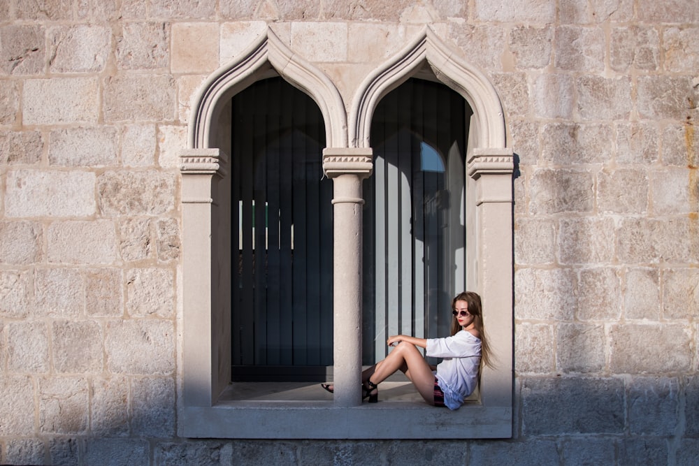 woman sitting on concrete window during daytime