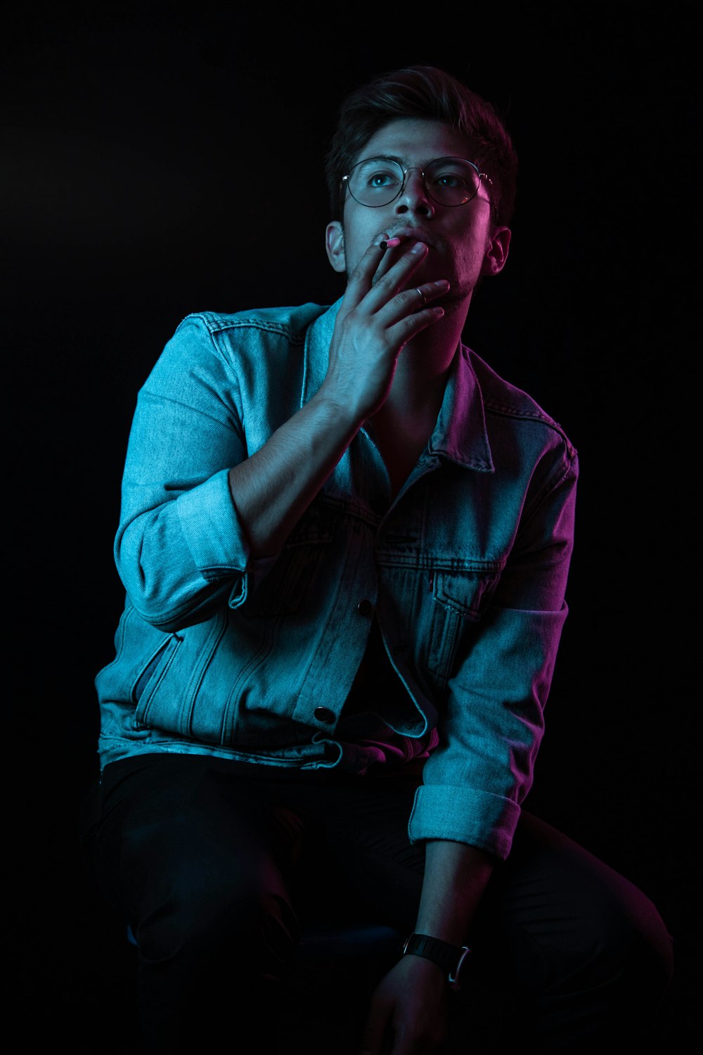 man wearing blue denim button-up jacket smoking cigarette