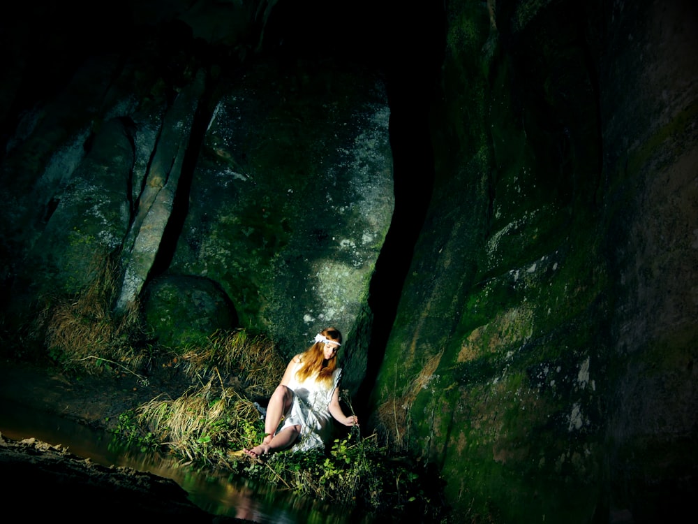 woman wearing gray dress sitting beside body of water inside cave