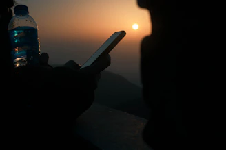 Lifestyle shot of a person holding the ivory-colored bottle with phone attached, standing by the beach at sunset.