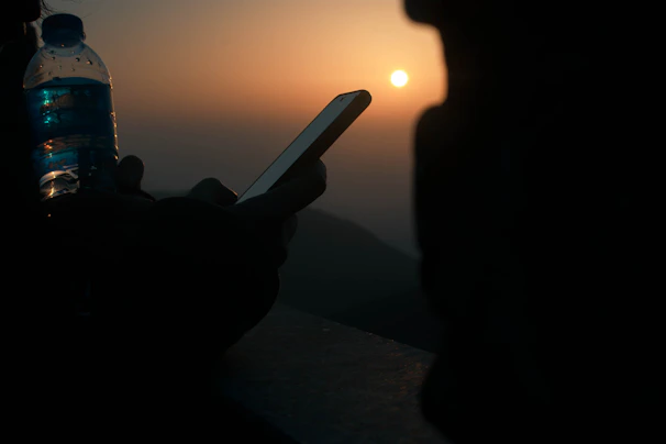 Lifestyle shot of a person holding the ivory-colored bottle with phone attached, standing by the beach at sunset.