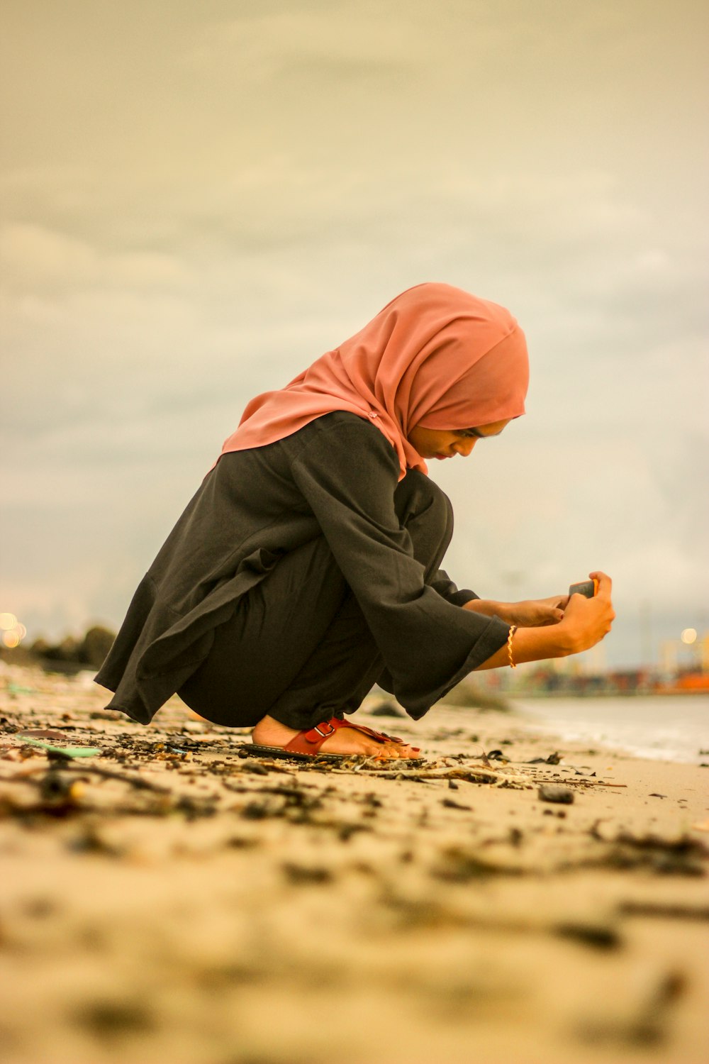 woman wearing black araba dress and orange hijab almost sitting on ground touching stone