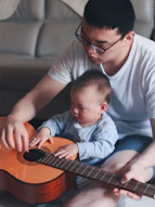 man wearing white crew-neck shirt beside baby holding guitar