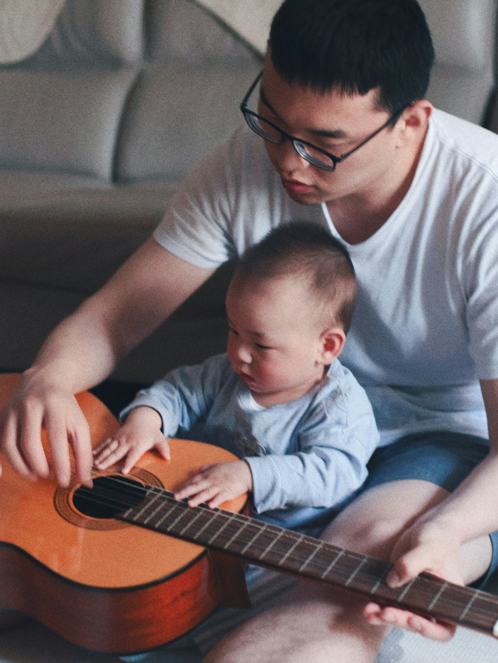 man wearing white crew-neck shirt beside baby holding guitar