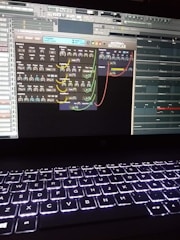 A computer screen displays a digital audio workstation with various audio controls and modules visible. The screen is filled with plugins and mixer settings for music production. Below the screen, a laptop keyboard is visible, illuminated by a backlight.