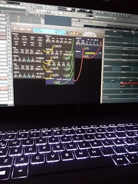 A computer screen displays a digital audio workstation with various audio controls and modules visible. The screen is filled with plugins and mixer settings for music production. Below the screen, a laptop keyboard is visible, illuminated by a backlight.