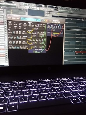 A computer screen displays a digital audio workstation with various audio controls and modules visible. The screen is filled with plugins and mixer settings for music production. Below the screen, a laptop keyboard is visible, illuminated by a backlight.
